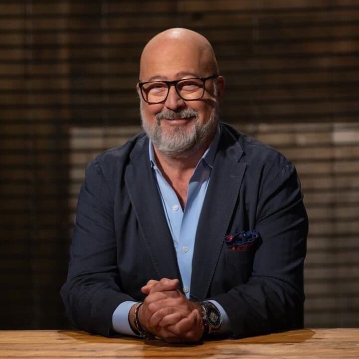 Bald man with glasses and grey beard, wearing a navy blazer and light blue shirt.